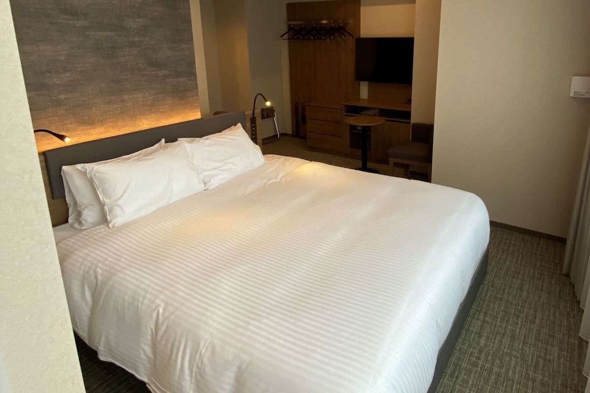 A hotel room with a large bed, a desk, a chair, a flat-screen TV, and a wooden cabinet.