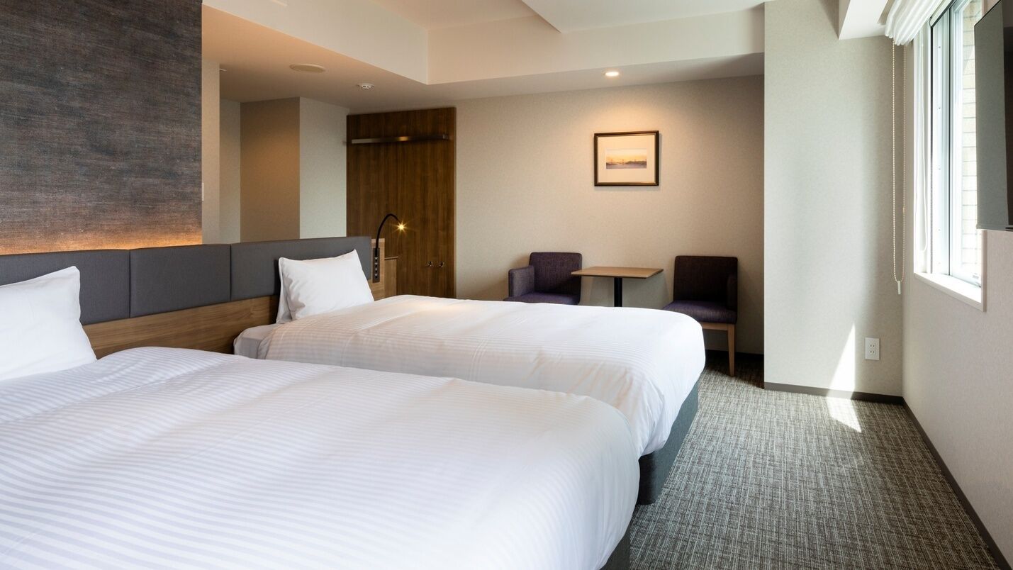 A hotel room with two beds, a desk, and a chair.