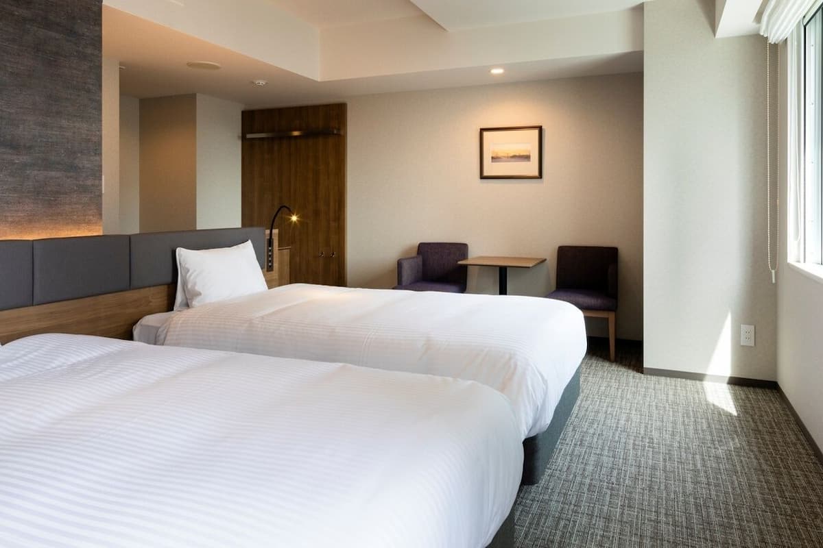 A hotel room with two beds, a desk, and a chair.