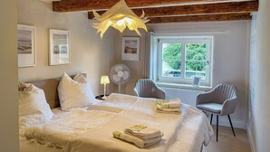 Een slaapkamer met een bed, een ventilator, een raam en een stoel.