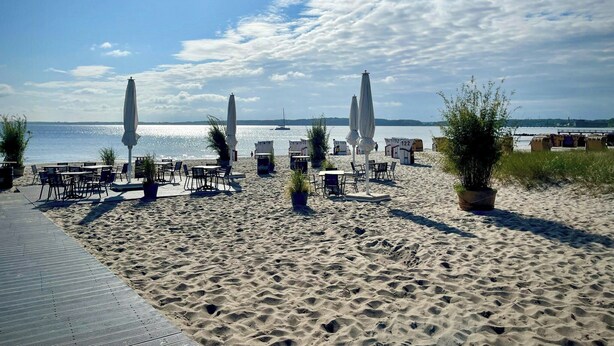 Een strandgebied met terrasplekken, parasols en uitzicht op zee.
