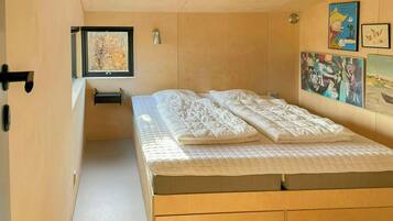 A bedroom with a bed, a window, a wall-mounted light, and artwork.