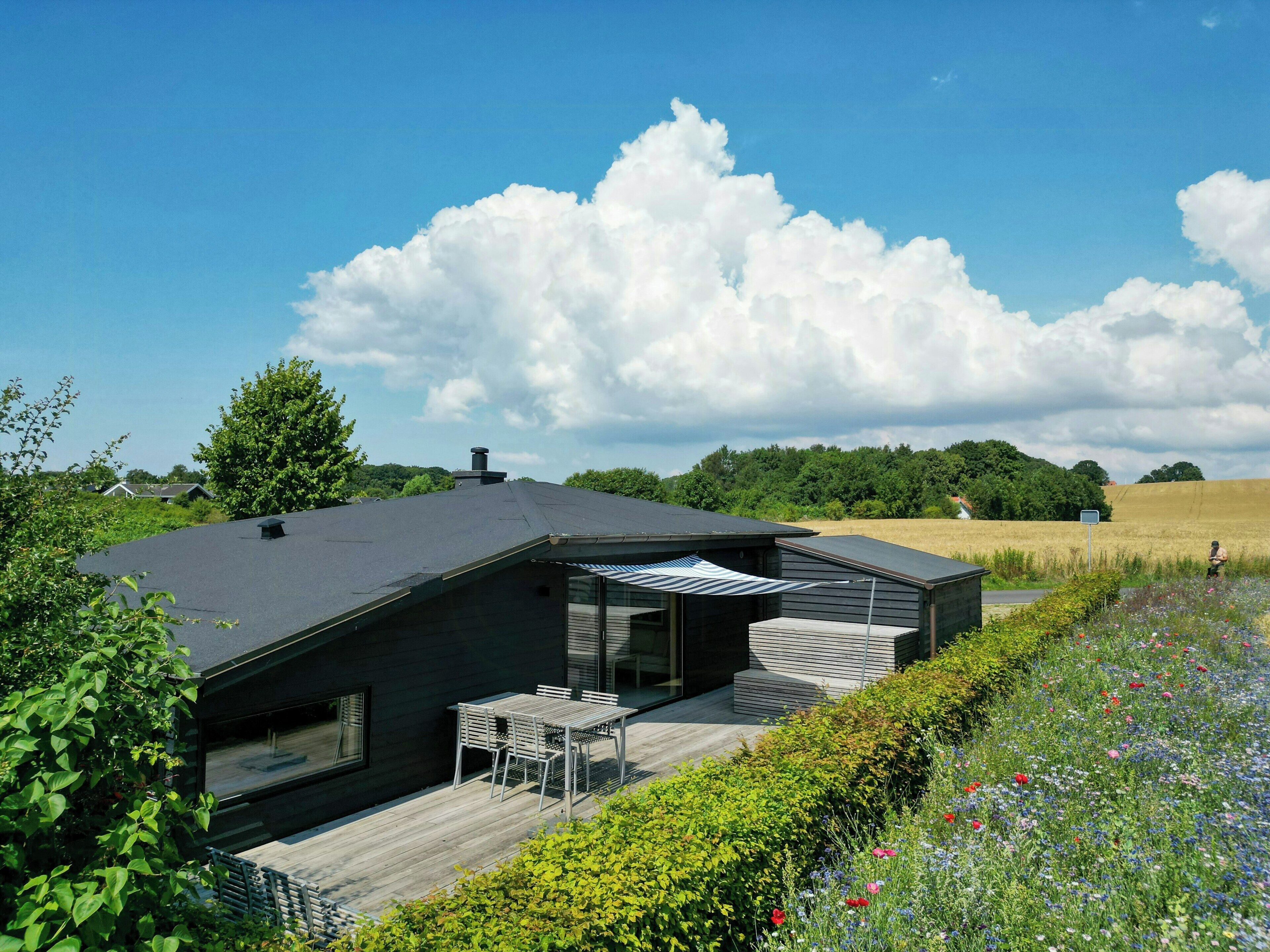 Ein modernes Haus mit einer Terrasse, einem überdachten Sitzbereich und Blick auf ein Feld.