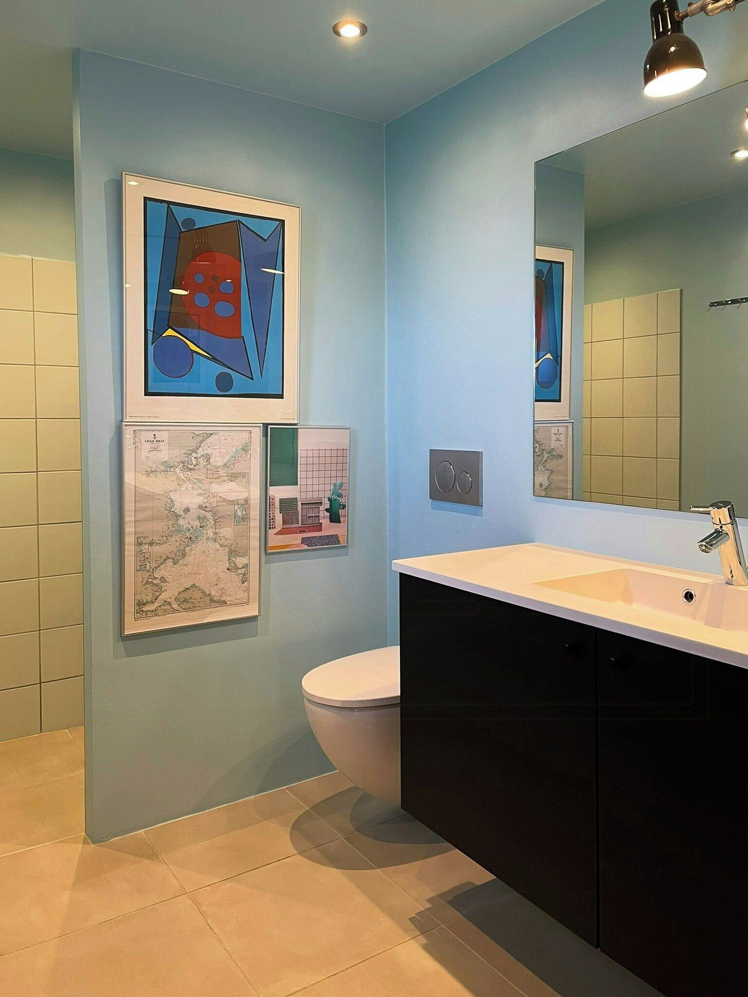 Een moderne badkamer met een wastafel, spiegel en toilet. Er hangen kunstwerken in lijsten aan de muur.