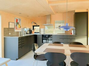 A modern kitchen with a central island, a dining table with chairs, and artwork on the walls. - Holiday home with view of Helnæs Bay (Haarby)