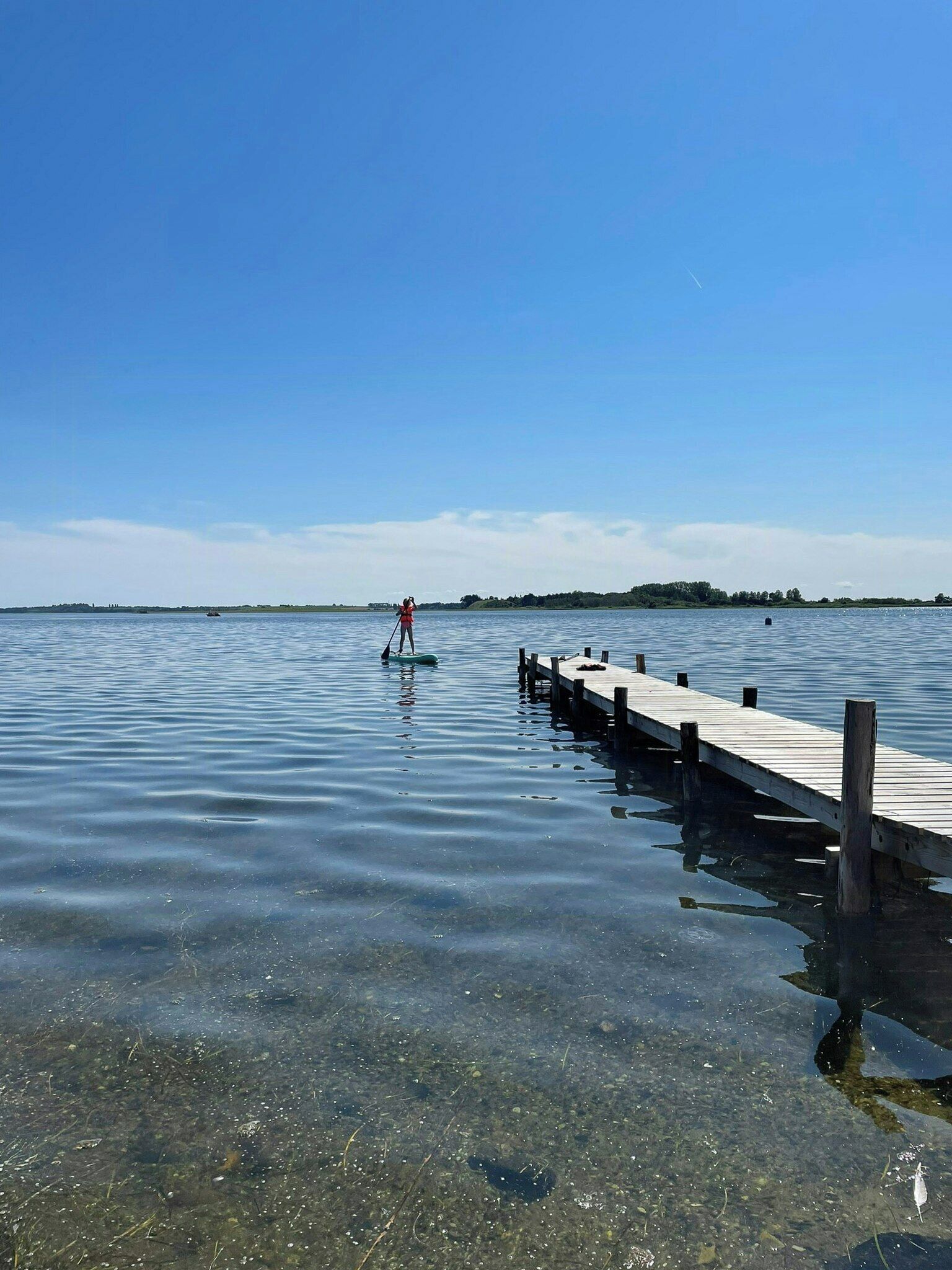 Una vista despejada de un lago tranquilo con un muelle de madera que se adentra en el agua.