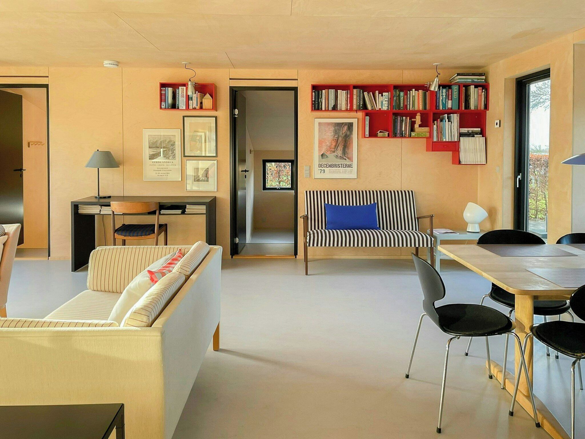 A modern living space with a sofa, a striped bench, a dining table with chairs, a bookshelf, and framed pictures on the walls.