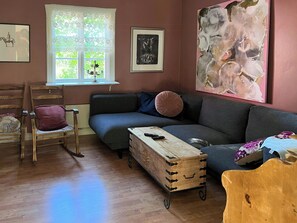 A living room with a sofa, a wooden chair, a small table, and a window with a view of greenery. - Cultural cottage by Lake Fryken in Värmland (Östra Ämtervik)