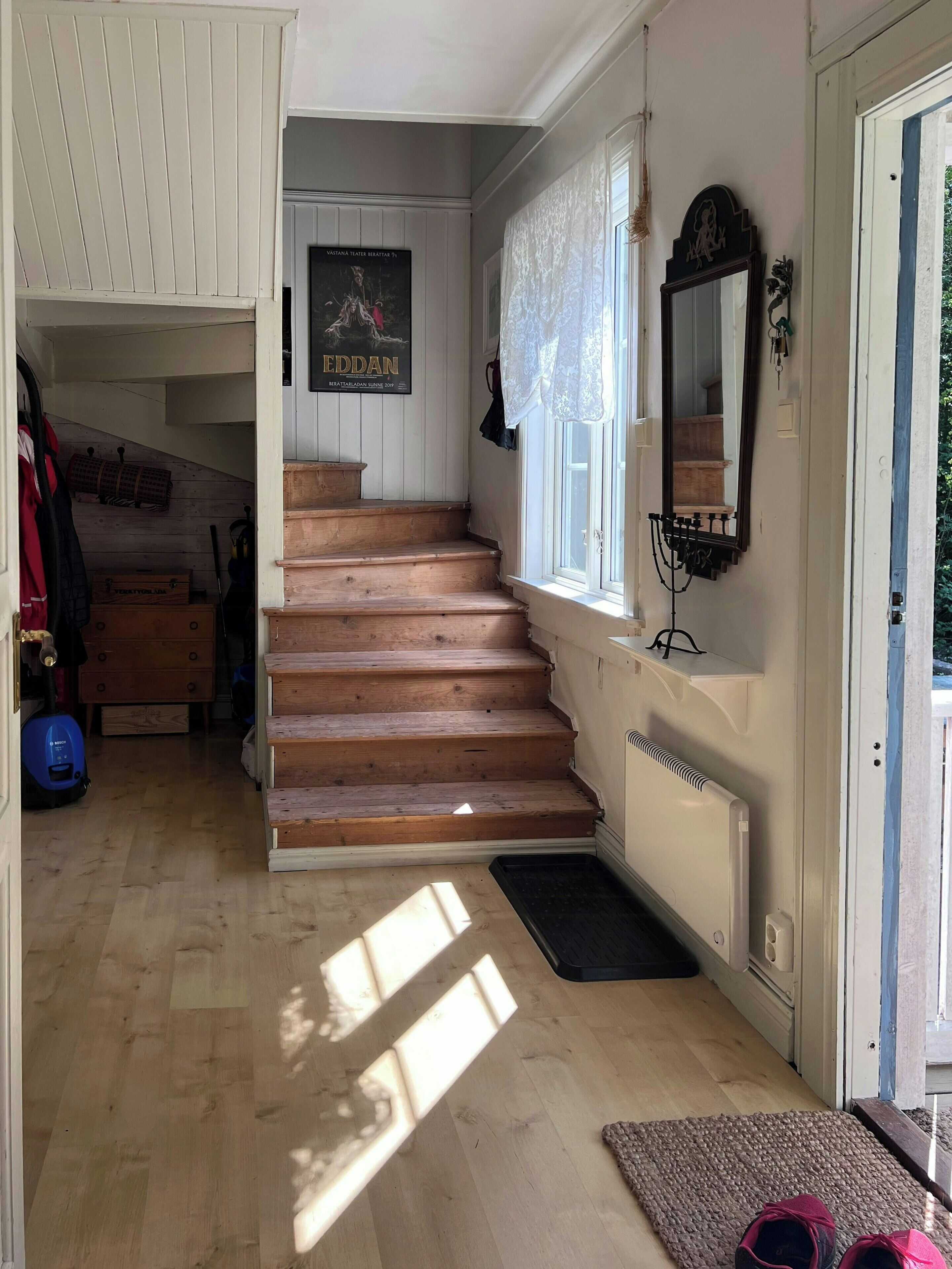 Un escalier menant à un deuxième étage, un radiateur, une porte avec un miroir et une affiche accrochée au mur.