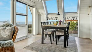A dining area with a table, chairs, and a view through large windows. - Summer house with panoramic sea views on Røsnæs (Kalundborg)