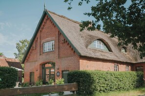 Ein rotes Backsteinhaus mit einem Reetdach, einem Holzzaun und einer gepflegten Hecke.