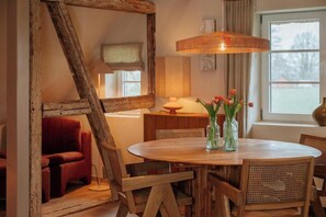 Ein Essbereich mit einem runden Holztisch, zwei Stühlen, einer Blumenvase, einer Lampe und einem Fenster mit Vorhängen.