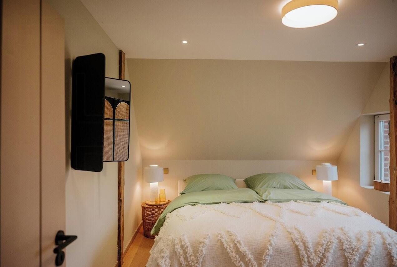 Ein Schlafzimmer mit einem Bett, zwei Nachttischlampen, einem Wandspiegel und einer Tür.