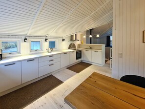 Eine moderne Küche mit weißen Schränken, einem Holztisch und Blick ins Freie durch Fenster.