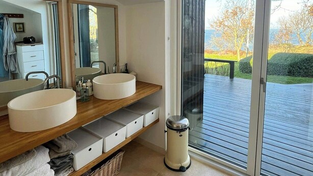 A modern bathroom with two sinks, a large mirror, and a view of a deck and trees. - Architect-designed house with private beach (Løgstrup)