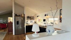 A modern kitchen with a central island, a refrigerator, and a dining area with a red sofa. - Architect-designed house with private beach (Løgstrup)