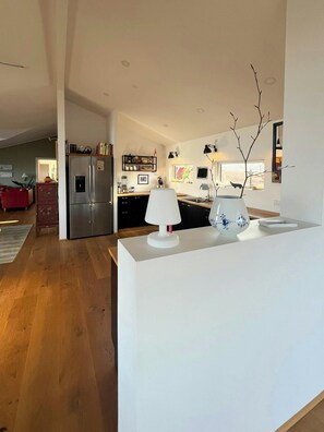 A modern kitchen with a central island, a refrigerator, and a dining area with a red sofa. - Architect-designed house with private beach (Løgstrup)