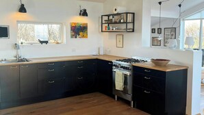 A modern kitchen with a large island, dark cabinetry, and a gas stove. - Architect-designed house with private beach (Løgstrup)