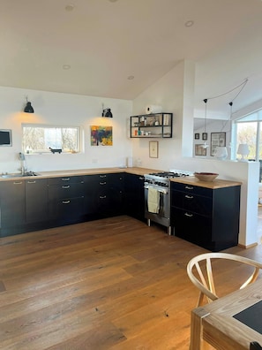 A modern kitchen with a large island, dark cabinetry, and a gas stove. - Architect-designed house with private beach (Løgstrup)
