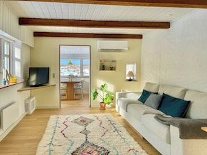 Ein Wohnzimmer mit Sofa, Fernseher, Essbereich mit Tisch und Stühlen sowie Blick durch eine Tür.