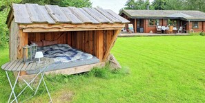 Una baita di legno rustica con un piccolo portico, un tavolo e delle sedie, e un prato erboso.