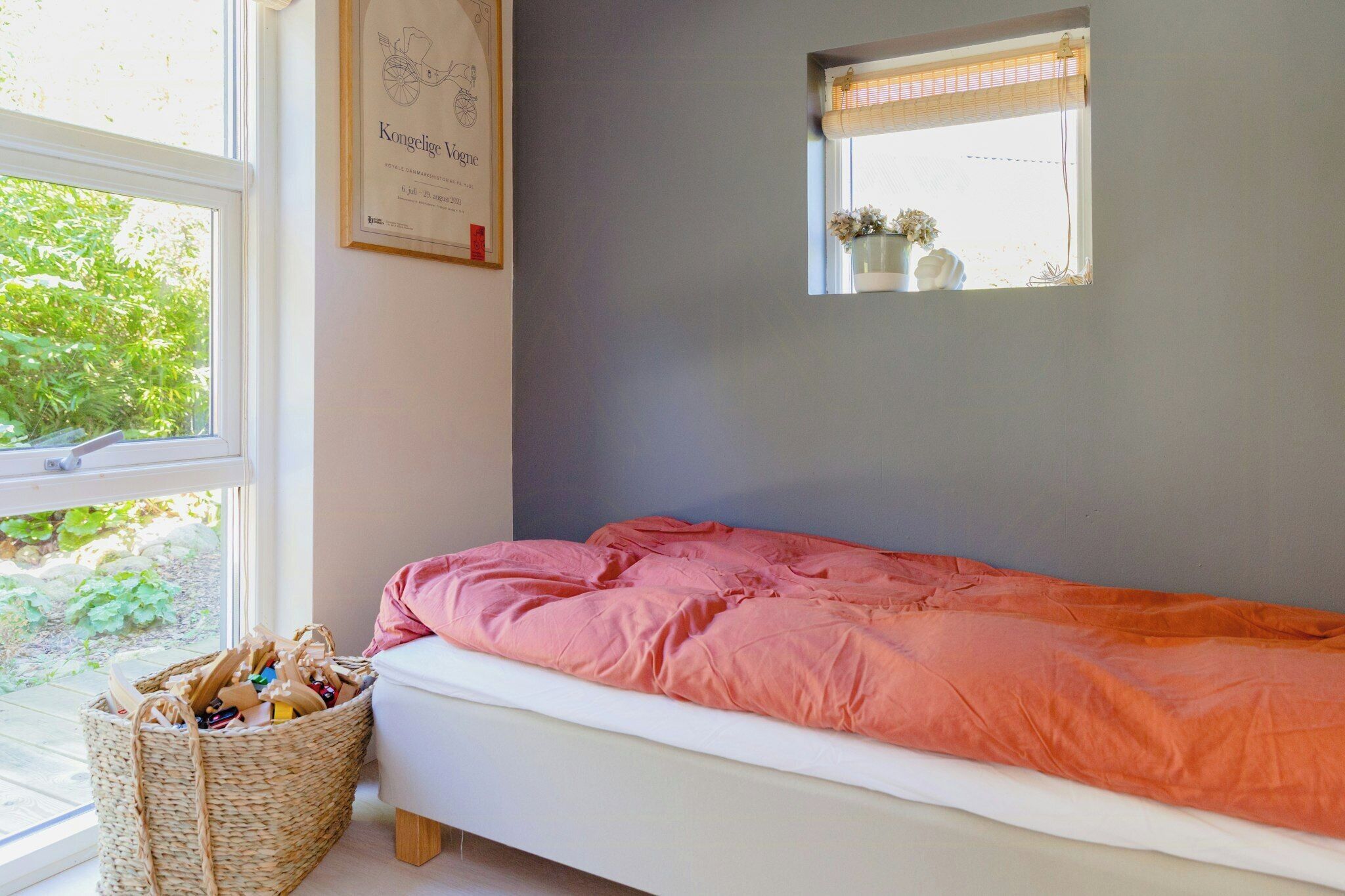 Quarto com cama, janela, prateleira pequena e cesta.