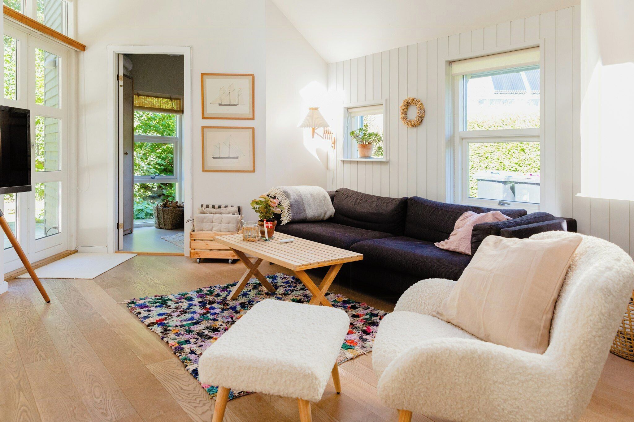A cozy living room with a dark-colored sofa, a white armchair, a wooden coffee table, and a colorful rug.