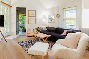 A cozy living room with a dark-colored sofa, a white armchair, a wooden coffee table, and a colorful rug. - An intimate get-away by the Sandvig bay (Haderslev)
