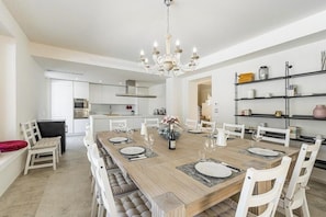 A modern dining area with a wooden table, white chairs, and a chandelier. - Luxury villa with pool in Aso Valley (Monterubbiano)