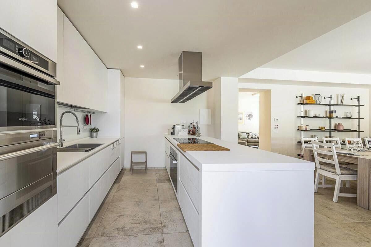 A modern kitchen with built-in appliances, a central island, and a dining area with chairs.