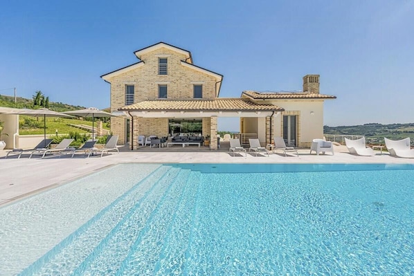 A large building with a swimming pool, lounge chairs, and a covered patio area. - Luxury villa with pool in Aso Valley (Monterubbiano)