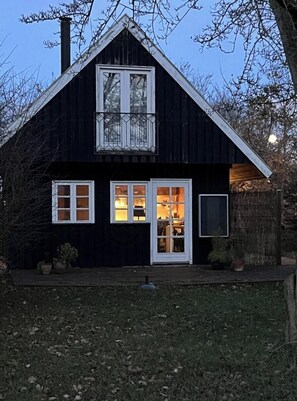 Une maison à deux étages, à l’extérieur sombre, avec des éléments décoratifs blancs et une cheminée bien visible.