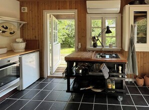 Une cuisine compacte dotée d’un plan de travail en bois, d’une cuisinière, d’un évier et d’une fenêtre donnant sur un paysage verdoyant.