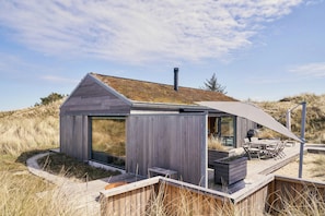 A modern beach house with a large glass window, a deck, and a covered outdoor seating area.