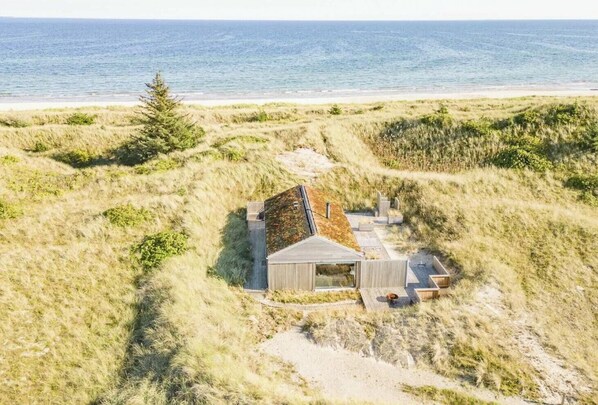 A coastal property with a small building, a sandy path, and a view of the sea.