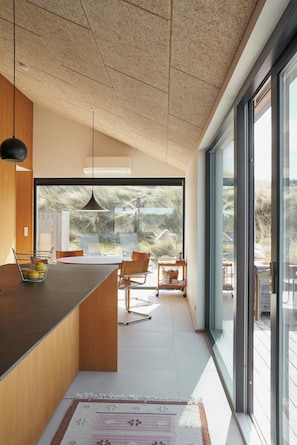 A modern kitchen with a large island, a dining area with chairs, and a view through glass doors.
