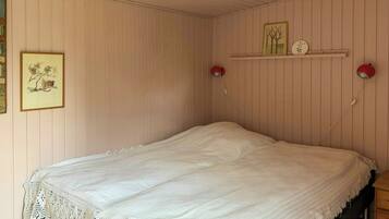 Una cama individual con una manta blanca de punto, una lámpara de pared roja y un cuadro en la pared.