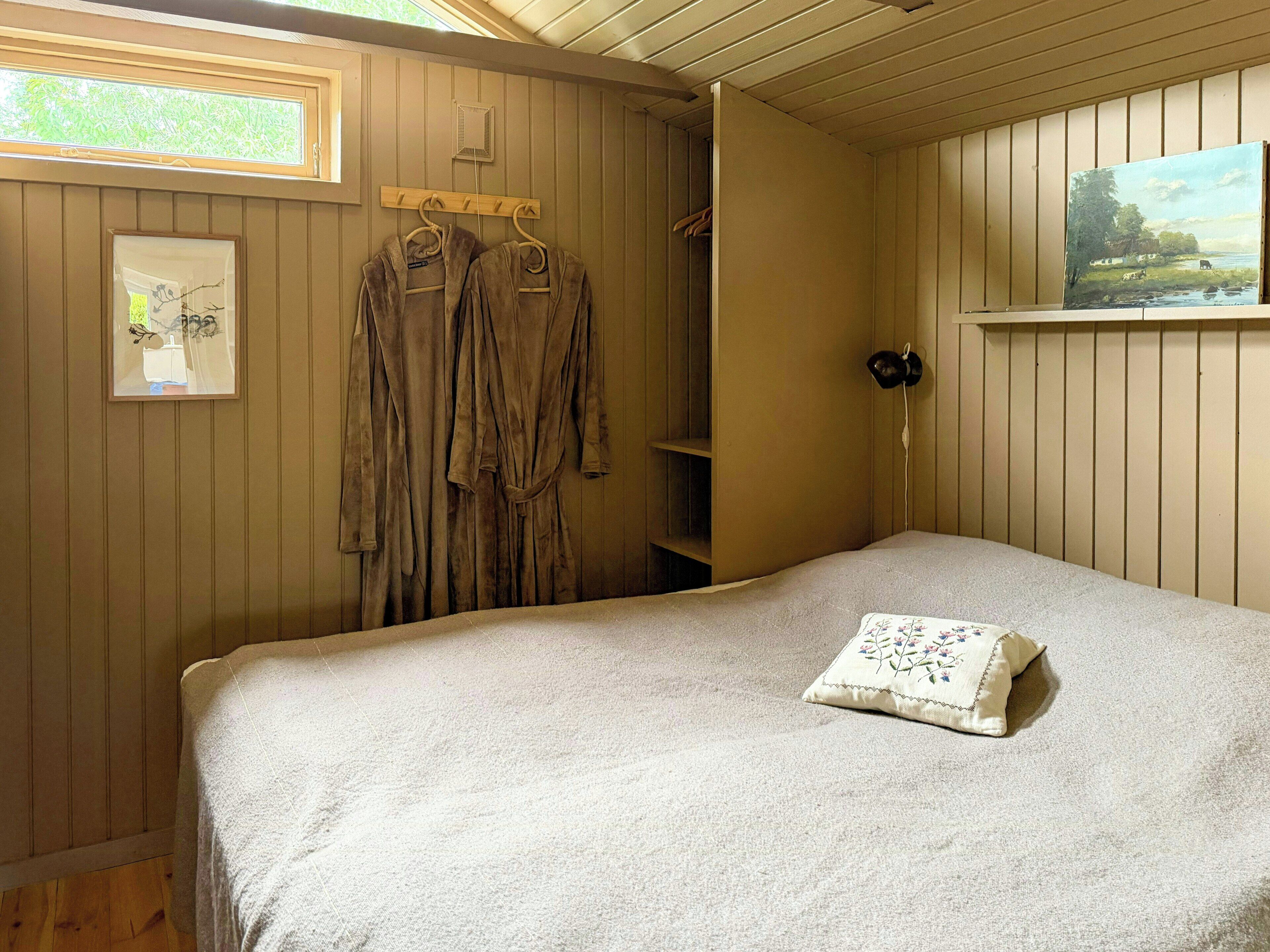 A room with a bed, a robe rack, a painting, and a window.