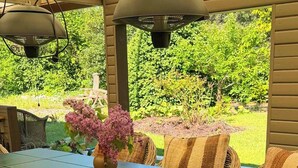 A covered patio with a dining table, wicker chairs, and a potted plant.