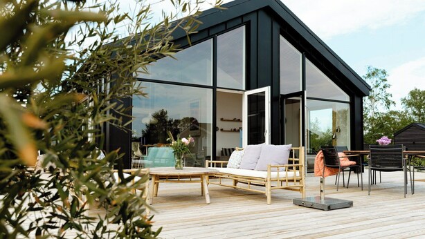 A modern house with a deck, a sofa, and a dining table. - Newly built summer house with sea view (Haderslev)
