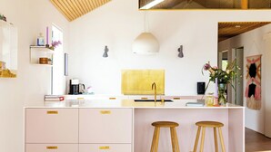 A modern kitchen with a central island, white cabinetry, and a wooden ceiling. - Newly built summer house with sea view (Haderslev)