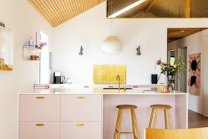 A modern kitchen with a central island, white cabinetry, and a wooden ceiling. - Newly built summer house with sea view (Haderslev)