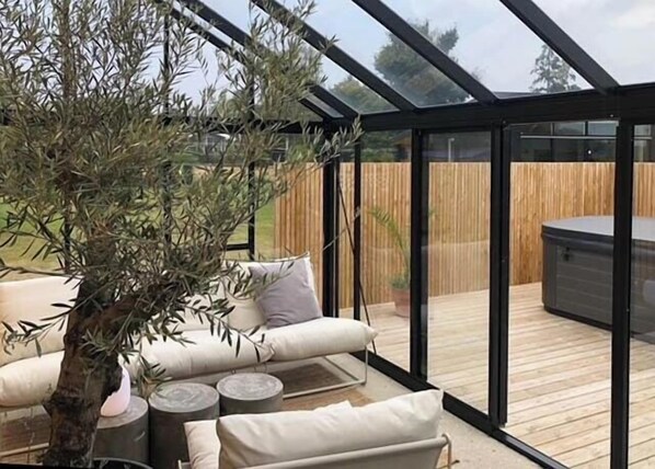 A covered patio with a seating area, a tree, and a hot tub.