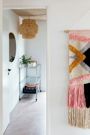 A hallway with a hanging woven light fixture, a metal shelving unit with items, and a wall-mounted tapestry.