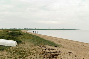 A sandy beach with a boat and grass in the foreground, and a calm body of water extending to the horizon.