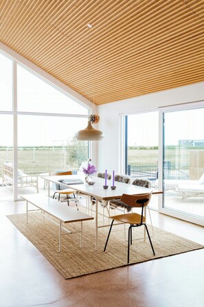 A modern dining area with a wooden ceiling, large windows, and a view of the outdoors. - Newly built summer house with sea view (Haderslev)