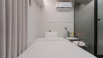 Habitación de hotel con cama, mesita de noche con lámpara, unidad de aire acondicionado y puerta de cristal.