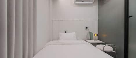 Habitación de hotel con cama, mesita de noche con lámpara, unidad de aire acondicionado y puerta de cristal.