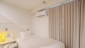 Una habitación de hotel con cama, escritorio y silla, aire acondicionado y ventana con cortinas.