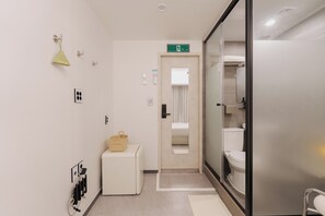 A hotel bathroom with a toilet, a sink, a mirror, a towel rack, and a small storage unit.